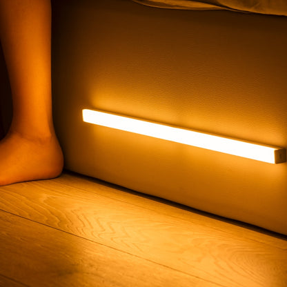 Réglette LED blanc chaud allumée sous un lit, éclairant le sol la nuit